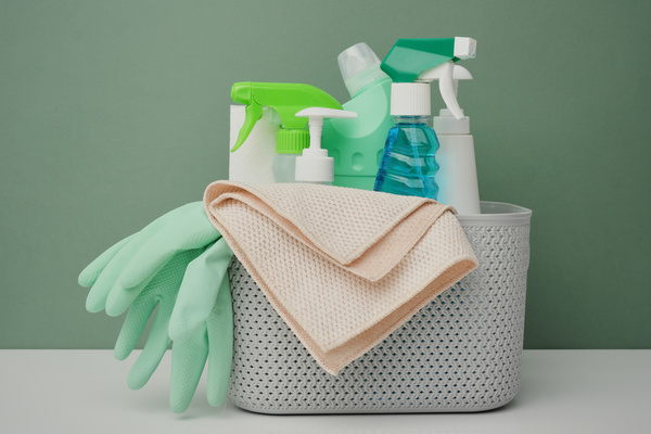Dispensers and sprayers with detergents in a plastic basket with green rubber gloves and light microfiber